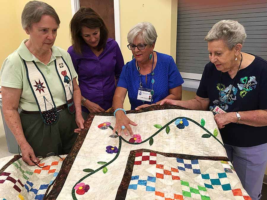 four women admiring the details on a quilt