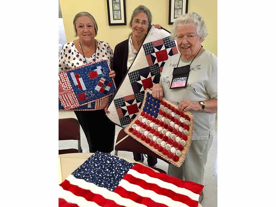three women displaying their quilts