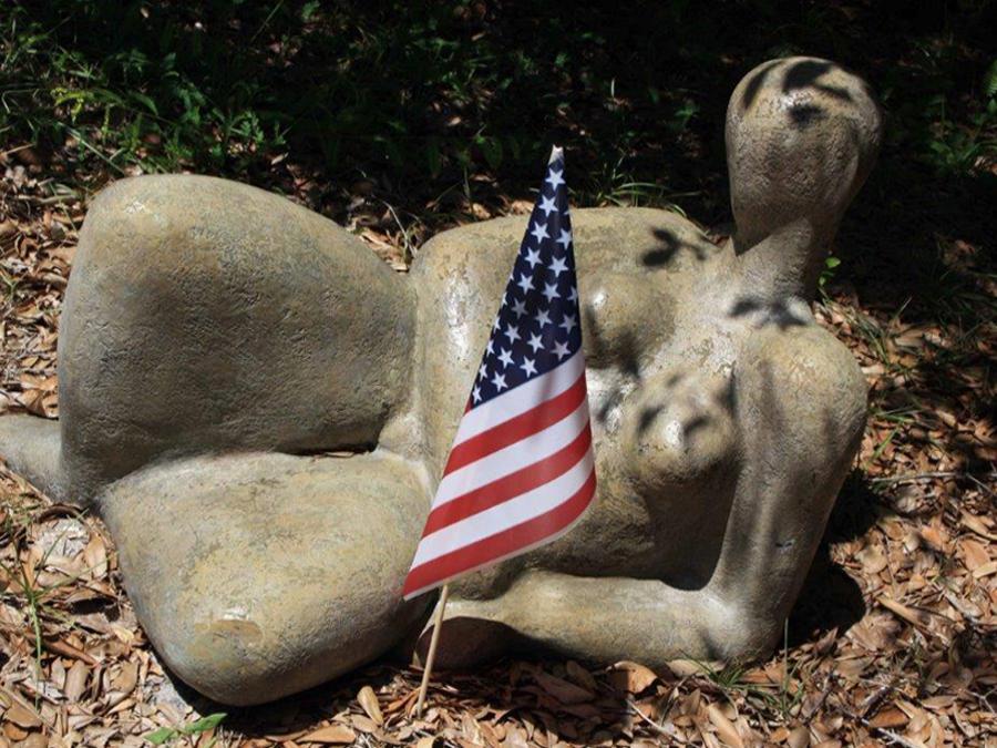 sculpture with humane form outside with American flag next to it